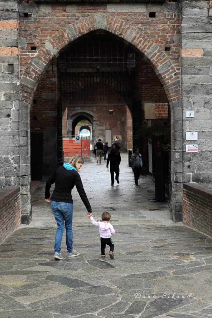 Mother walking through the drawbridge of the Sforza Castle in Milan Italy with a toddler. Things to do in Milan.
