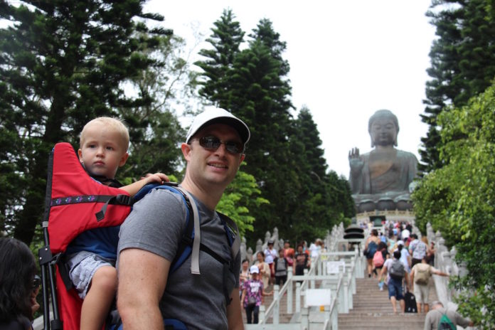 Father wears a baby on his back as he hikes up to big Buddha in Hong Kong