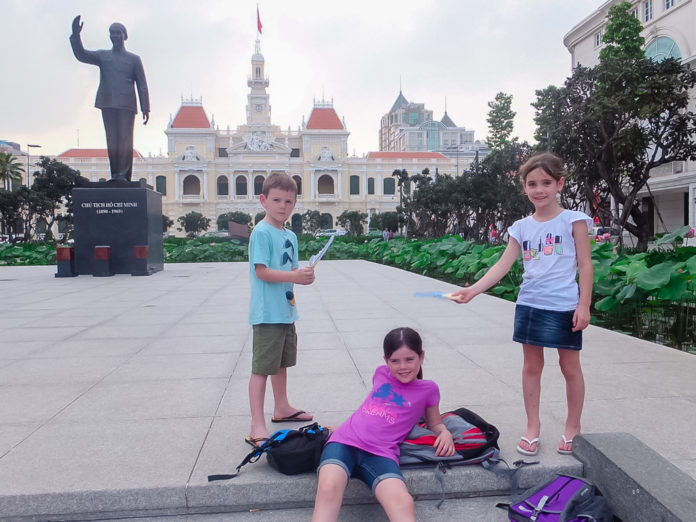Three kids having fun in a public square. Fresh influenced architecture can be seen in the distance.