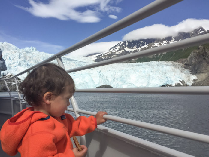 Toddler holds onto railing and takes in the ice capped view in Seward, Alaska