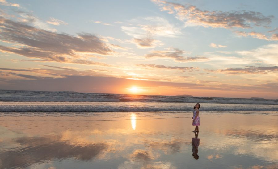 Girl stands on a beach in Goa watching the colourful and reflective sunset