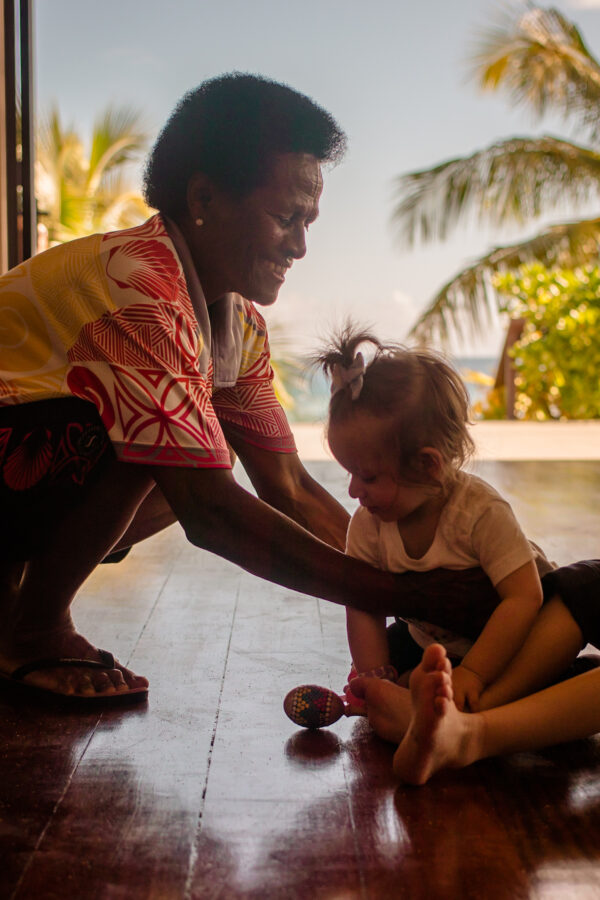 Smiling kids club employee lifts a toddler off the ground at a family friendly resort in Fiji. 